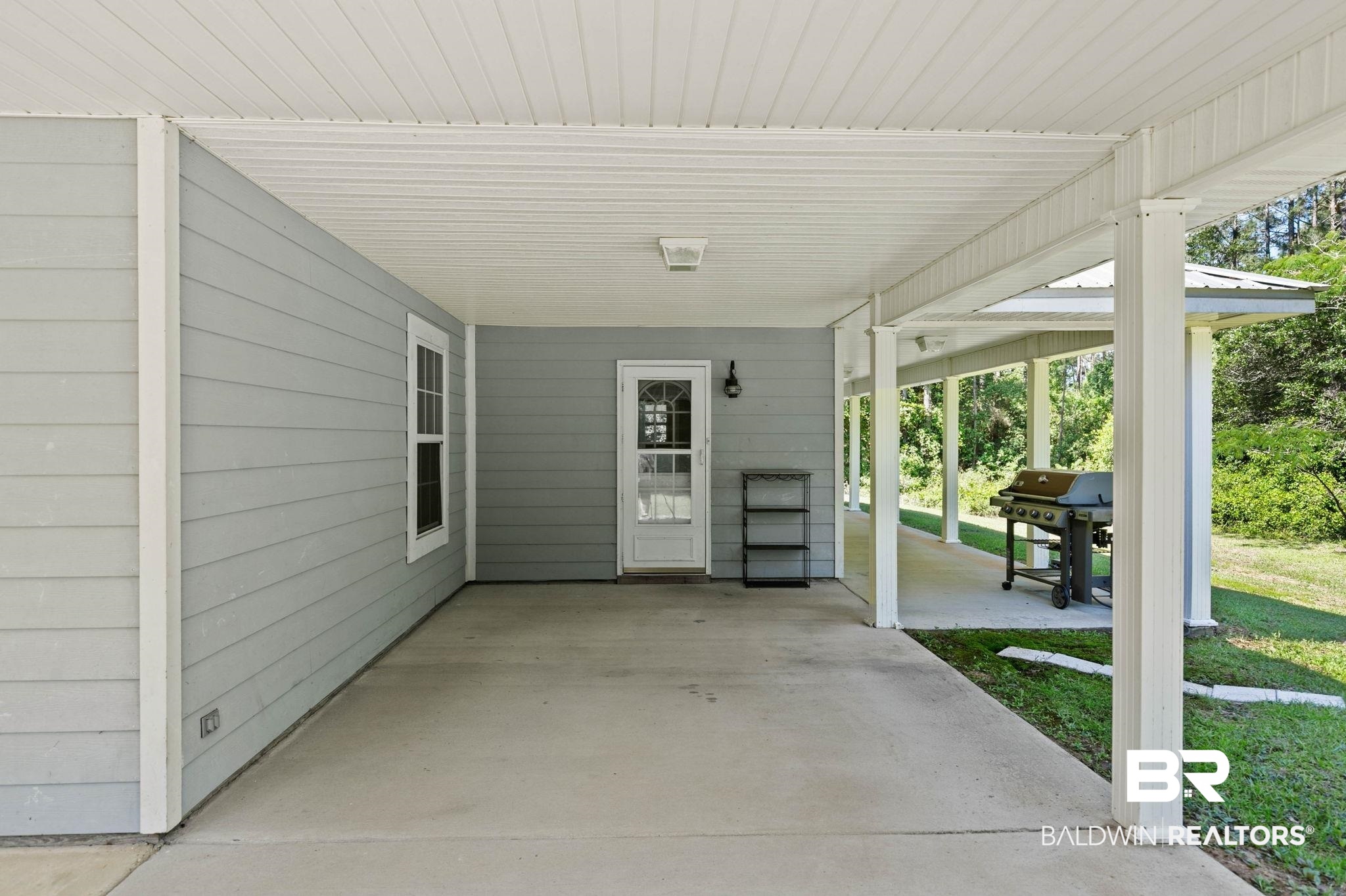 20219 Greek Cemetery Road Robertsdale, AL 36567 - Photo 33 of 41 Covered concrete patio featuring light gray siding, white trim, and an exterior door with a decorative glass insert