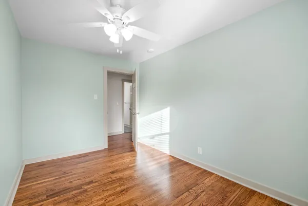 a view of an empty room with wooden floor and a ceiling fan