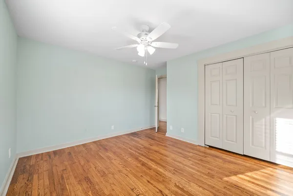 a view of an empty room with wooden floor and a ceiling fan