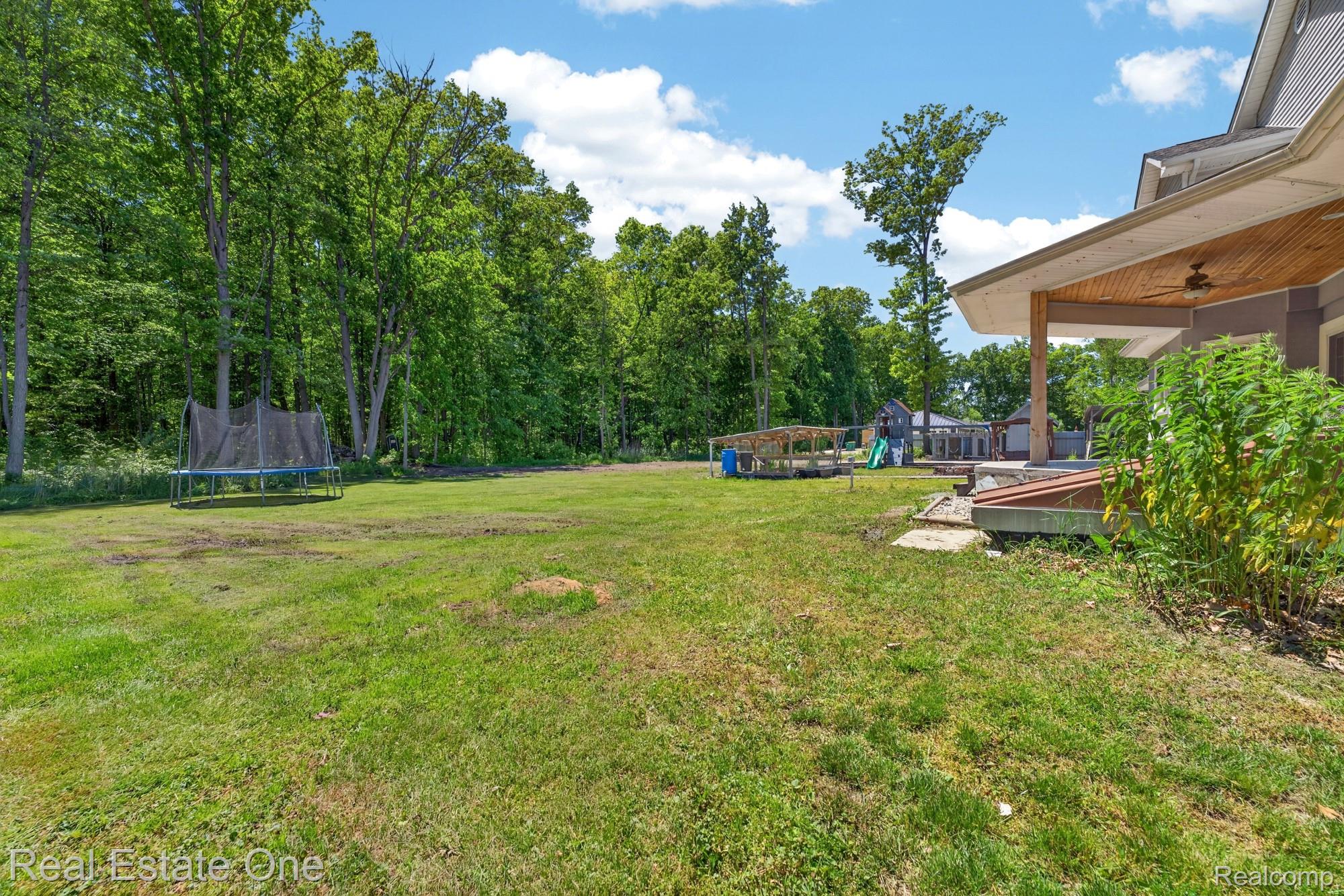 26987 Crawford Road Romulus, MI 48174 - Photo 43 of 51 Expansive green lawn surrounded by mature trees, featuring a covered patio with a wood-finish ceiling, an outdoor ceiling fan, and a built-in deck