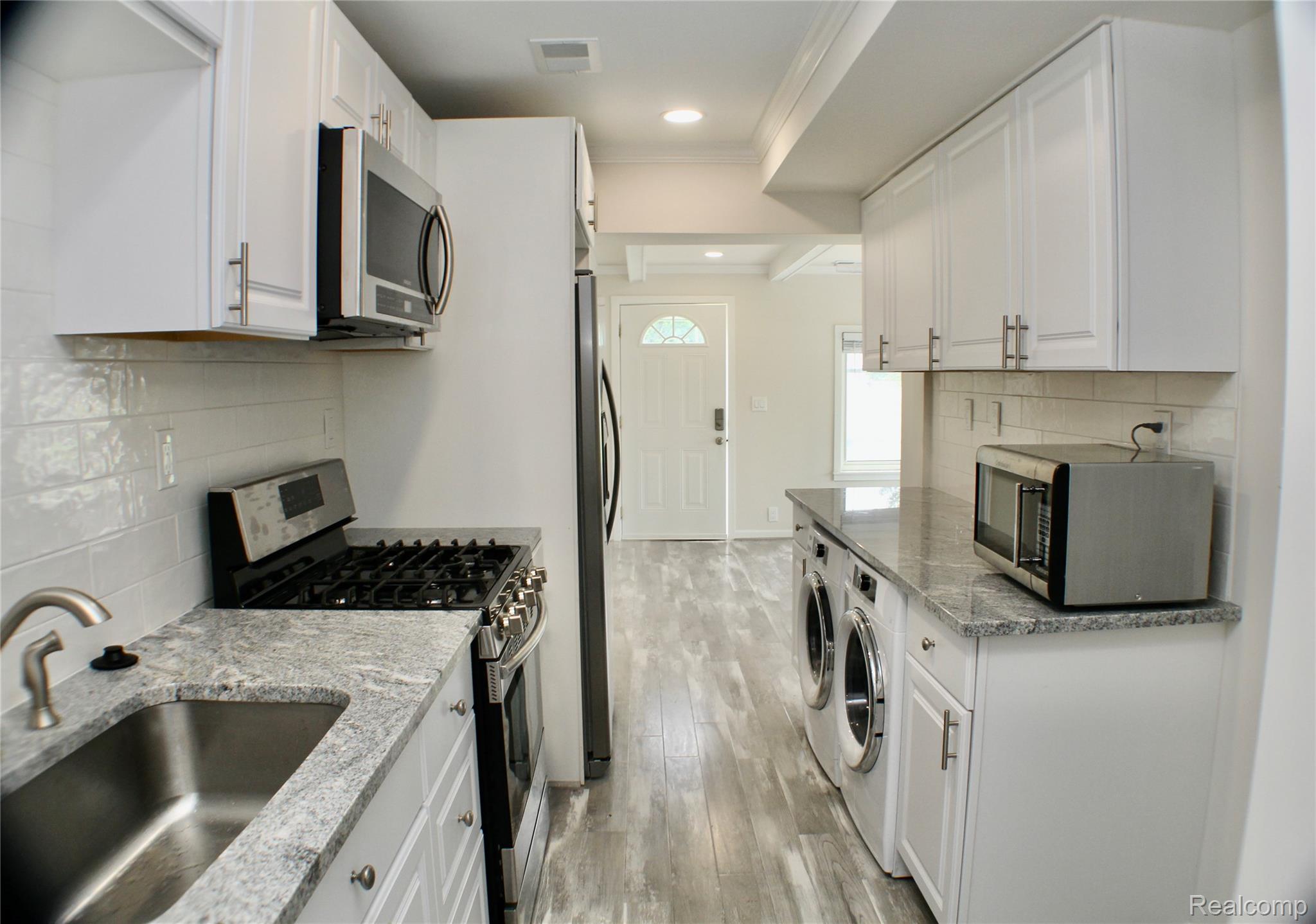 48677 Sugarbush Road, Unit 1 New Baltimore, MI 48047 - Photo 7 of 10 Kitchen featuring white shaker-style cabinetry, stainless steel appliances, a subway tile backsplash, and light-toned wood-finish flooring