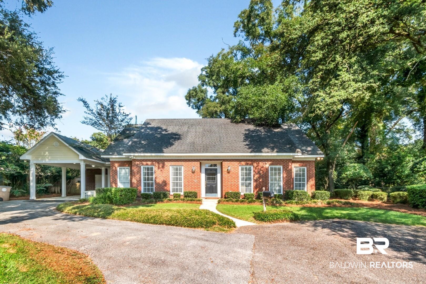 Cape cod-style house featuring asphalt driveway, brick siding, an attached carport, and a front lawn