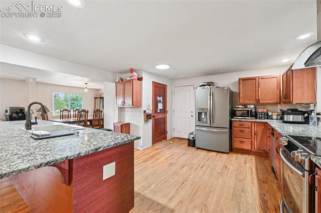 1263 York Road Colorado Springs, CO 80918 - Photo 7 of 29 Kitchen with light stone countertops, stainless steel appliances, brown cabinets, light wood-style flooring, and exhaust hood