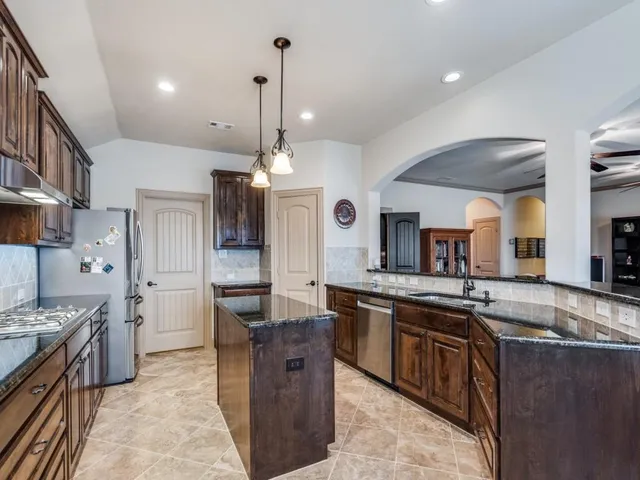 a large kitchen with stainless steel appliances kitchen island granite countertop a stove a sink dishwasher and a wooden cabinets