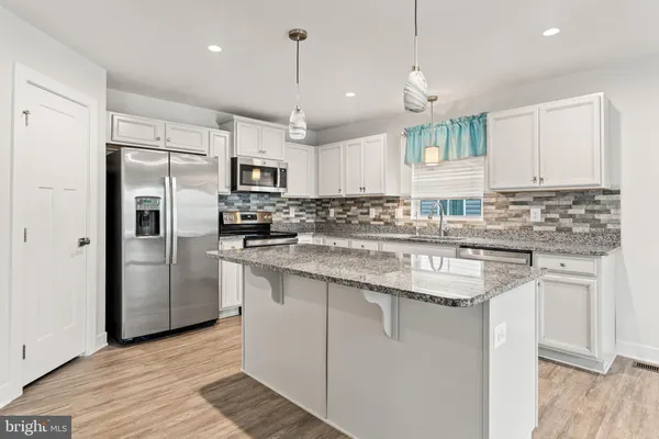 a kitchen with stainless steel appliances granite countertop a sink a stove a refrigerator and island with wooden floor