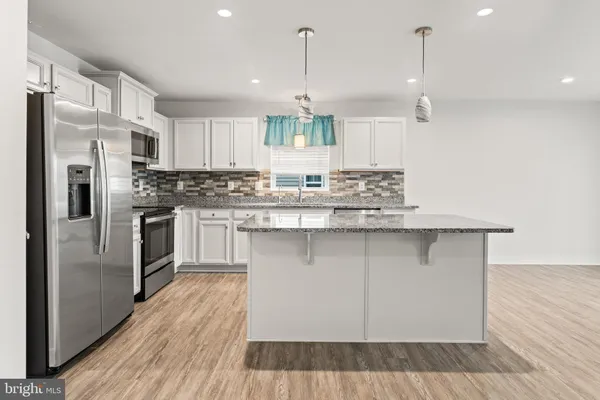 a kitchen with stainless steel appliances granite countertop a sink a stove a refrigerator and island with wooden floor