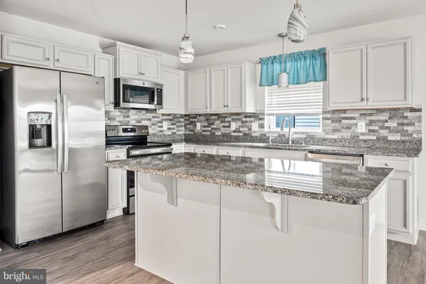 a kitchen with stainless steel appliances granite countertop a sink a refrigerator a center island a stove and a wooden floor