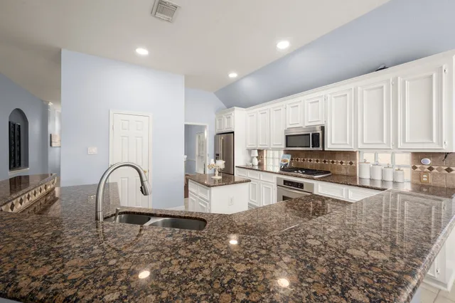 a large kitchen with stainless steel appliances granite countertop a stove a sink a refrigerator and white cabinets with wooden floor