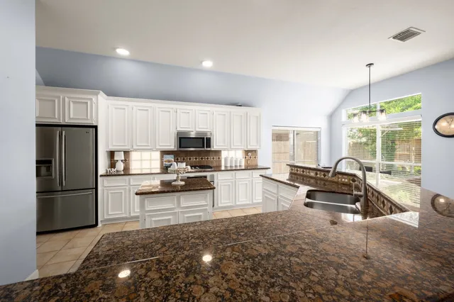 a kitchen with stainless steel appliances kitchen island granite countertop a refrigerator stove top oven and sink with wooden floor