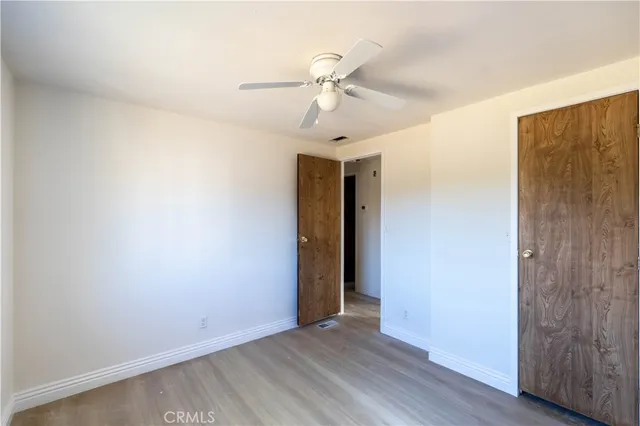 a view of an empty room with wooden floor and a ceiling fan