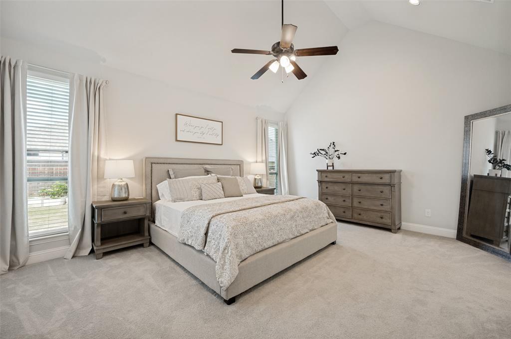 8440 Colburn The Colony, TX 75056 - Photo 11 of 34 Spacious primary suite featuring soaring vaulted ceilings, plush carpet, and large windows that fill the room with natural light. This private retreat offers ample space for a sitting area, creating a peaceful atmosphere to relax and unwind at the end of the day.