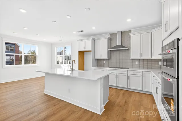 a large kitchen with stainless steel appliances granite countertop a stove a sink dishwasher and a oven with white cabinets