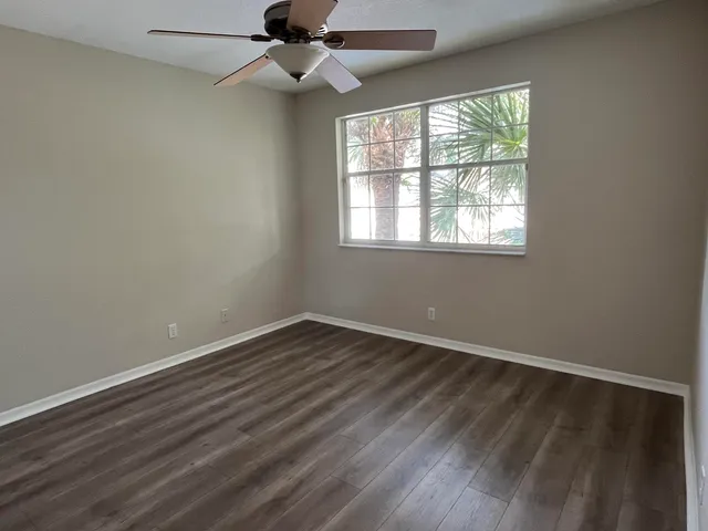 an empty room with wooden floor fan and windows