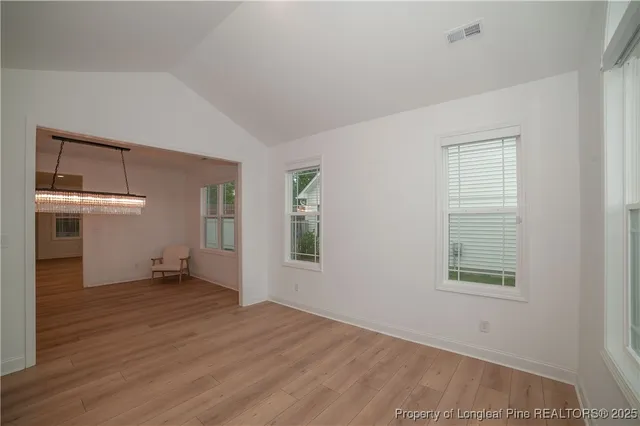 an empty room with wooden floor kitchen view and windows