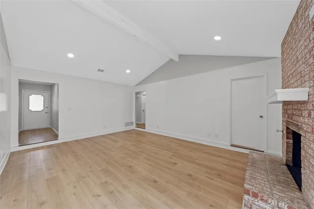 a view of an empty room with wooden floor and a fireplace