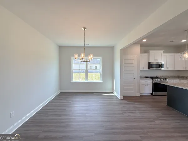 an empty room with wooden floor kitchen appliances and windows