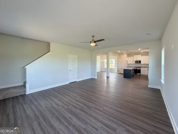 a view of an empty room and kitchen with wooden floor