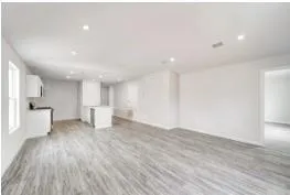a view of an empty room with wooden floor and a kitchen