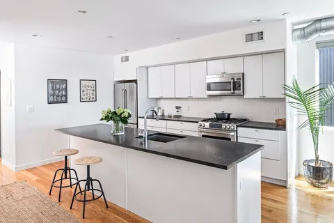 a kitchen with stainless steel appliances granite countertop a sink a stove a dining table and chairs with wooden floor