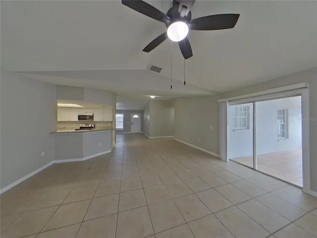 an empty room with chandelier fan and windows