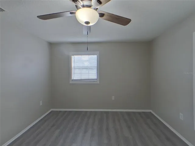 an empty room with a chandelier fan and wooden floor