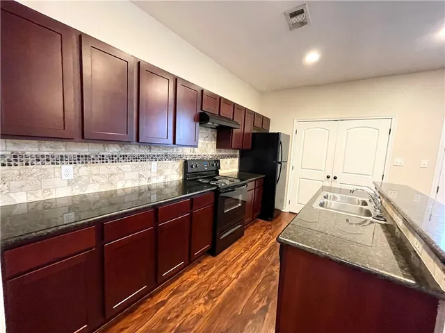 a large kitchen with stainless steel appliances granite countertop a stove and a wooden floors