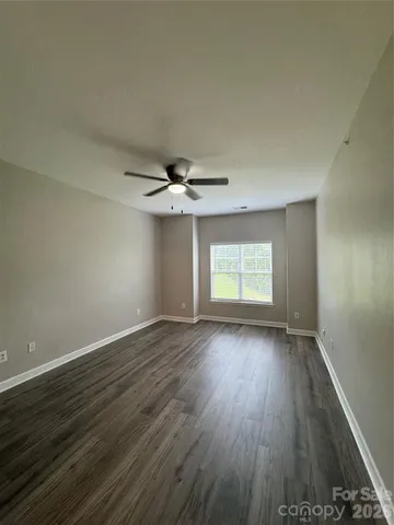 an empty room with wooden floor chandelier fan and windows