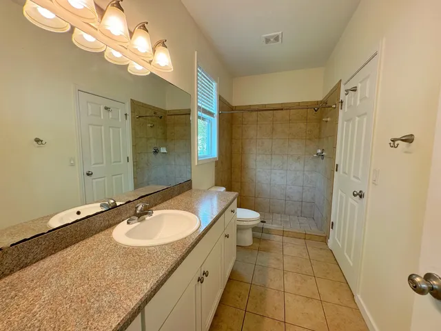 a bathroom with a granite countertop sink a toilet a mirror and shower