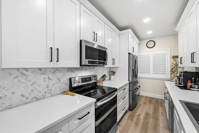 a kitchen with stainless steel appliances a sink a stove top oven a refrigerator cabinets and a dining table