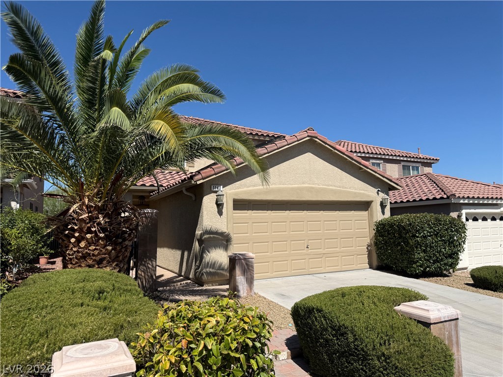 1141 Cathedral Ridge Street Henderson, NV 89052 - Photo 3 of 77 This residence features a warm stucco exterior with a tiled roof, complemented by lush landscaping.
