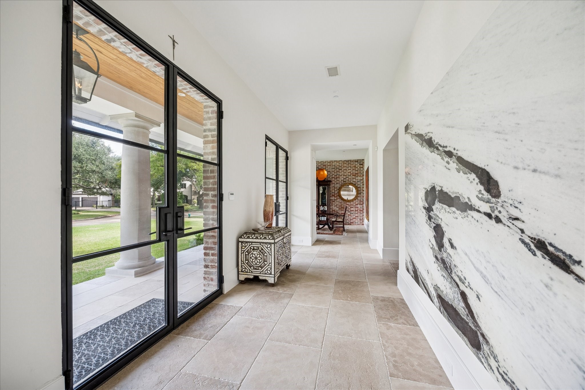 7 Hedwig Shadows Lane Houston, TX 77024 - Photo 11 of 46 Flooded with natural light, the entry corridor is lined with steel-framed glass doors and antique limestone floors, offering continuous sightlines to the front porch and gardens. A striking marble installation sets a sophisticated tone that carries throughout the home.