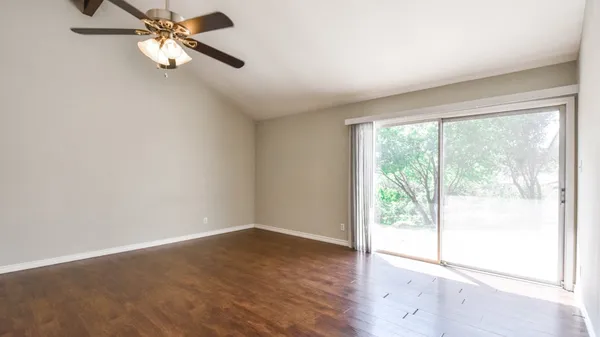an empty room with wooden floor fan and windows
