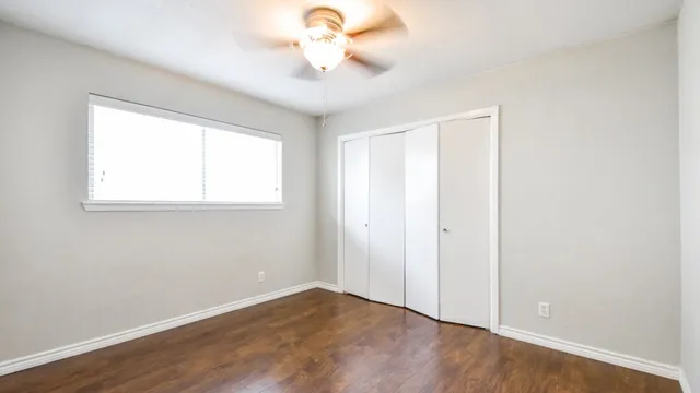 an empty room with wooden floor fan and windows