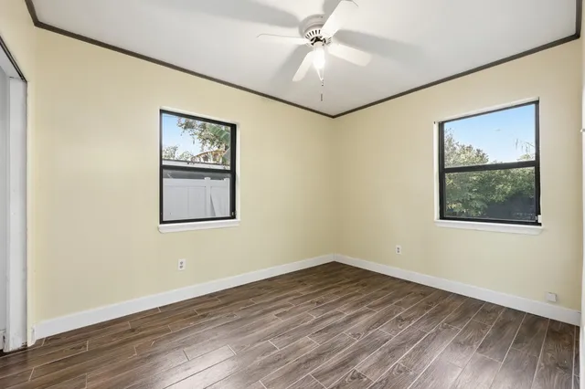 a view of an empty room with wooden floor and a ceiling fan