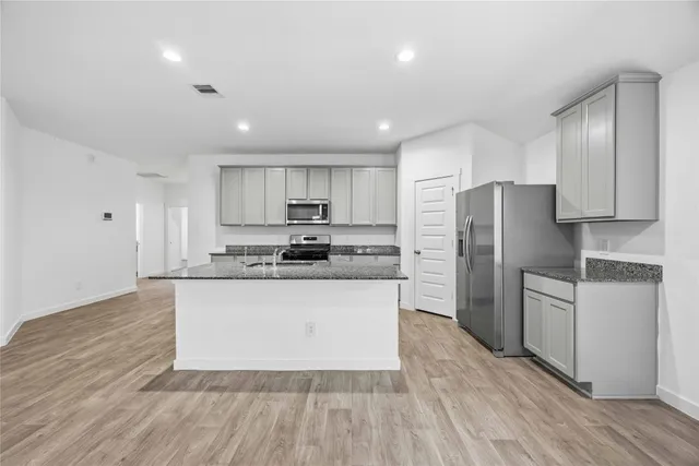 a kitchen with stainless steel appliances granite countertop a refrigerator a stove a sink and white cabinets with wooden floor