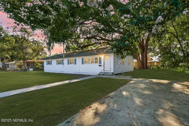 a view of a white house with a big yard and large trees