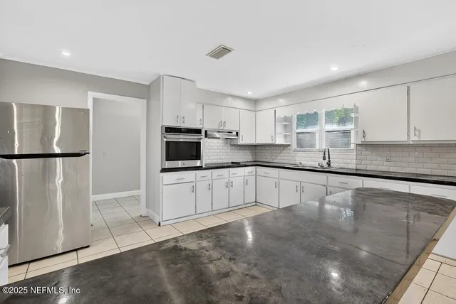 a large white kitchen with stainless steel appliances granite countertop a refrigerator a sink a stove a microwave and cabinets