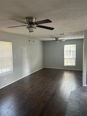 an empty room with wooden floor fan and windows