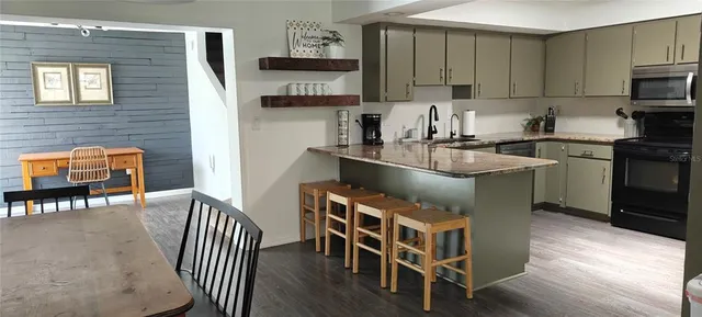 a kitchen with granite countertop kitchen island stainless steel appliances a dining table chairs sink and cabinets