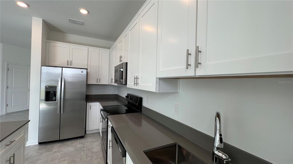 2396 Brook Marsh Loop Kissimmee, FL 34747 - Photo 11 of 29 a kitchen with stainless steel appliances granite countertop a refrigerator a sink a stove and white cabinets with wooden floor