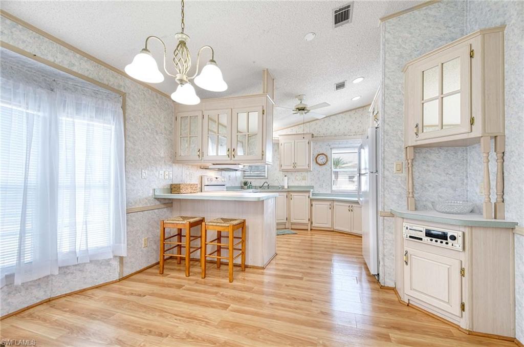 21 Onyx Drive, Unit 21O Naples, FL 34114 - Photo 6 of 30 Kitchen featuring a kitchen bar, light wood-type flooring, a textured ceiling, white refrigerator, and hanging light fixtures