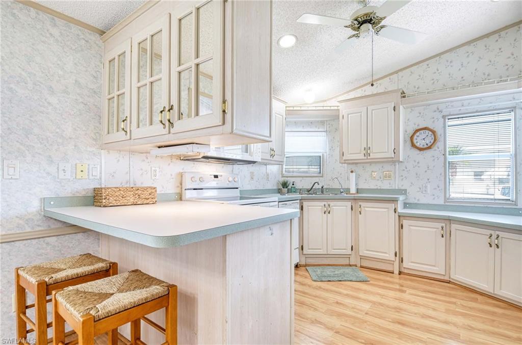 21 Onyx Drive, Unit 21O Naples, FL 34114 - Photo 7 of 30 Kitchen featuring white appliances, white cabinets, a textured ceiling, kitchen peninsula, and a breakfast bar area