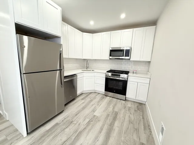 a kitchen with granite countertop a refrigerator a sink and white cabinets