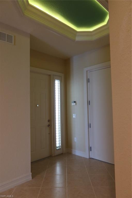 7168 Lemuria Circle, Unit 1701 Naples, FL 34109 - Photo 7 of 39 Foyer featuring a decorative tray ceiling with ambient lighting, a solid entry door with a full-length sidelight, ceramic tile flooring, and crisp white baseboards