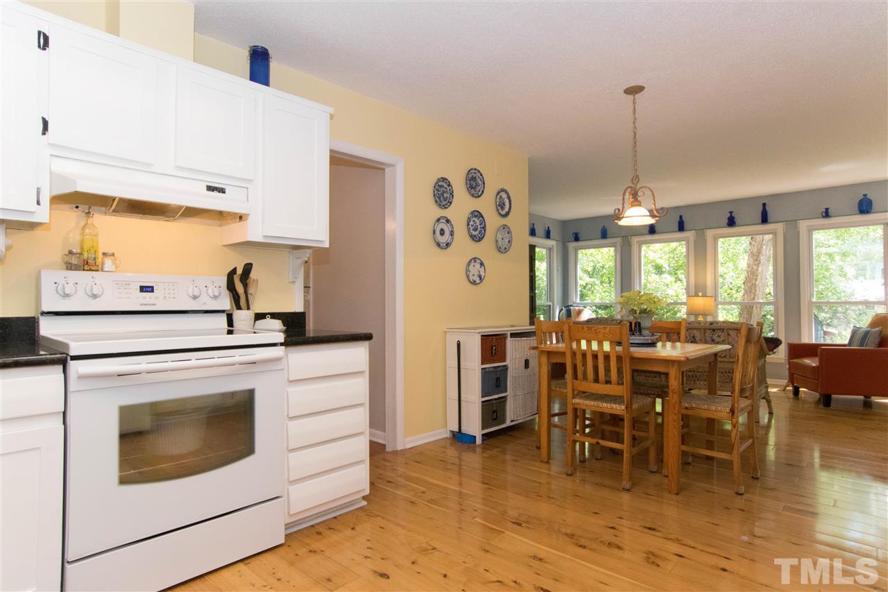 4708 Rampart Street Raleigh, NC 27609 - Photo 8 of 25 a kitchen with stainless steel appliances granite countertop a stove a dining table chairs and white cabinets with wooden floor