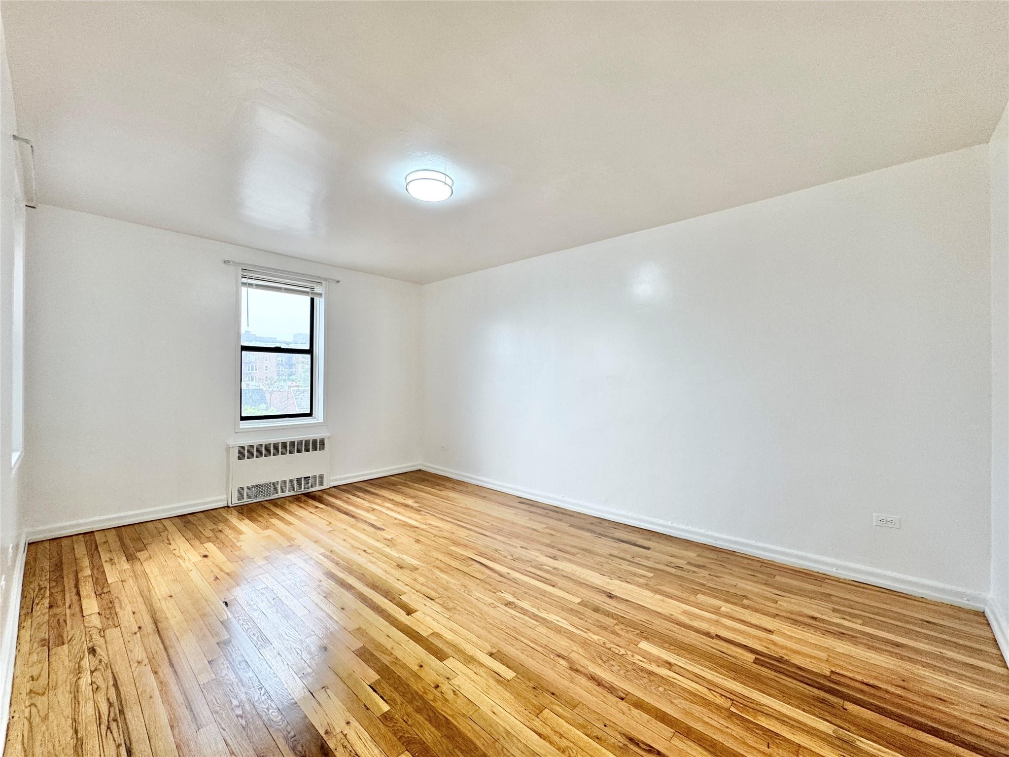 84-19 51st Avenue, Unit 4E Queens, NY 11373 - Photo 5 of 7 an empty room with wooden floor and windows