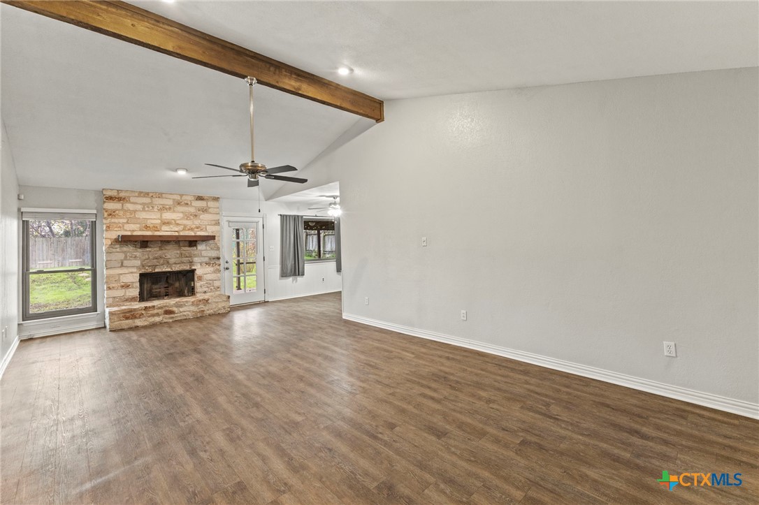 413 Suzzane Road Pflugerville, TX 78660 - Photo 6 of 23 Living room with wood finished floors, a stone fireplace, a beamed ceiling and a ceiling fan