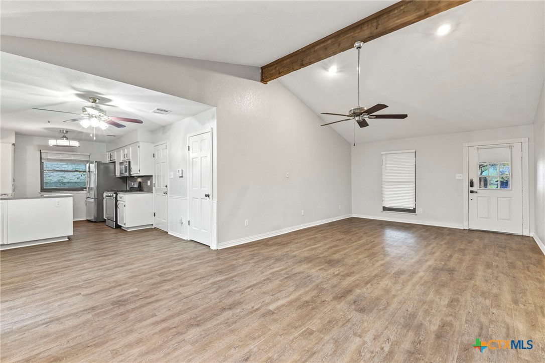 413 Suzzane Road Pflugerville, TX 78660 - Photo 7 of 23 Living room with wood finished floors, a stone fireplace, a beamed ceiling and a ceiling fan