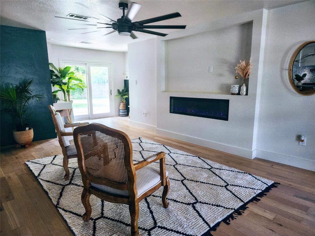 2908 Washington Street Commerce, TX 75428 - Photo 12 of 29 Spacious living area featuring wood-finish flooring, a built-in electric fireplace, sliding glass doors to the exterior, and a contemporary ceiling fan