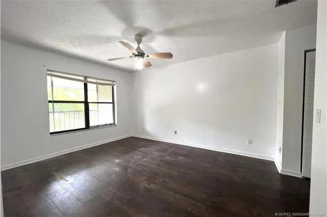 an empty room with wooden floor fan and windows